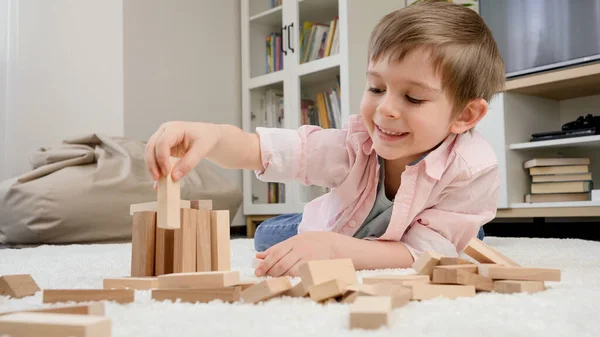 Милый маленький мальчик лежит на ковре и играет с игрушечными деревянными блоками. Концепция детского образования и игр на дому — стоковое фото