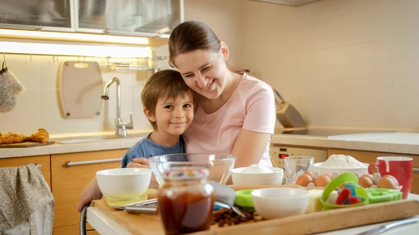 Felice madre ridente con il piccolo figlio che si abbraccia in cucina dopo aver cucinato il piatto. Bambini che cucinano con i genitori, piccolo chef, famiglia che ha tempo insieme, cucina domestica. — Foto Stock