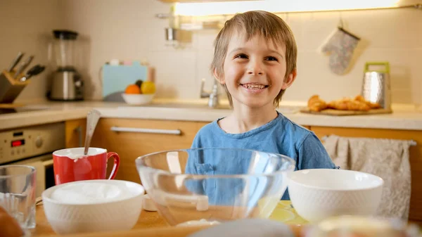 Funny laughing little boy eating creme for baking pie with spoon. Children cooking with parents, little chef, family having time together, domestic kitchen.