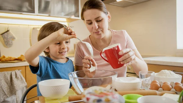 Giovane madre con piccolo figlio che versa gli ingredienti per la torta o la torta in una grande ciotola di vetro. Bambini che cucinano con i genitori, piccolo chef, famiglia che ha tempo insieme, cucina domestica. — Foto Stock