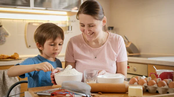 Маленький мальчик с молодой матерью проверяет и взвешивает ингредиенты на цифровых весах. Дети готовят с родителями, маленький шеф-повар, семья, проводящая время вместе, домашняя кухня. — стоковое фото