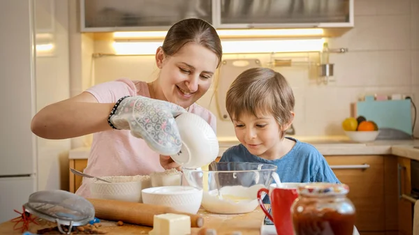 Mãe sorridente com filho pequeno derramando ovos em farinha e massa de mistura para torta ou bolo. Crianças cozinhar com os pais, pequeno chef, família ter tempo juntos, cozinha doméstica. — Fotografia de Stock