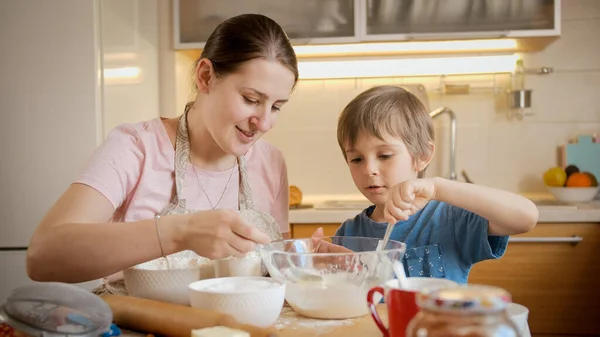 Madre felice con piccolo figlio mescolando e mescolando ingredienti di pasta in ciotola di vetro grande. Bambini che cucinano con i genitori, piccolo chef, famiglia che ha tempo insieme, cucina domestica. — Foto Stock