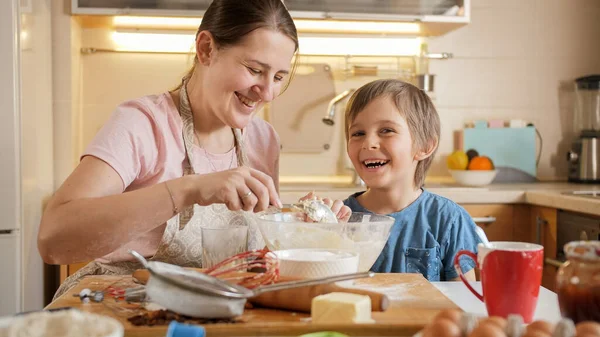 Szczęśliwy uśmiechnięty chłopiec całujący matkę podczas robienia ciasta w domu. Dzieci gotujące z rodzicami, mały kucharz, rodzina spędzająca razem czas, kuchnia domowa. — Zdjęcie stockowe