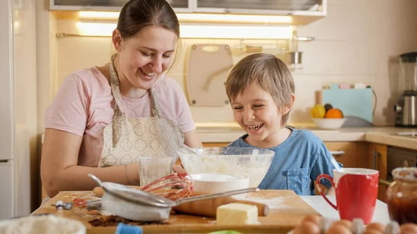 Szczęśliwy chłopak śmiejący się z matką bawiącą się i wygłupiającą podczas robienia ciasta na herbatniki w domu. Dzieci gotujące z rodzicami, mały kucharz, rodzina spędzająca razem czas, kuchnia domowa. — Zdjęcie stockowe