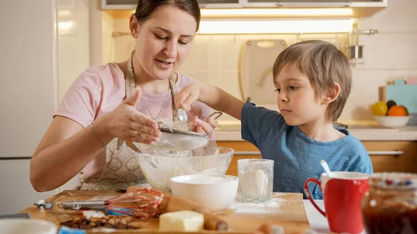 Liten pojke häller mjöl i såll för sållning och göra deg. Barn matlagning med föräldrar, liten kock, familj har tid tillsammans, kök. — Stockfoto