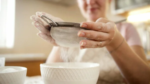 Closeup of young woman sifting flour through metal sieve on domestic kitchen — Stock Photo, Image