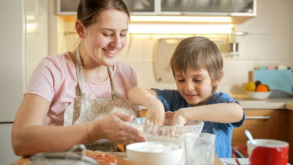 En liten pojke som hjälper sin mamma tjäna pengar och blandar dem med händer. Barn matlagning med föräldrar, liten kock, familj har tid tillsammans, kök. — Stockfoto