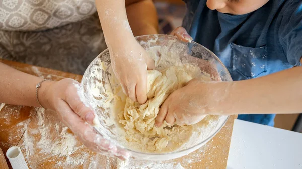 Крупный план маленького мальчика, месящего тесто в стеклянной миске на кухне — стоковое фото
