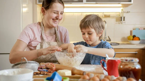 Buona madre sorridente con il piccolo figlio impastare e odorare pasta in ciotola di vetro. Bambini che cucinano con i genitori, piccolo chef, famiglia che ha tempo insieme, cucina domestica. — Foto Stock
