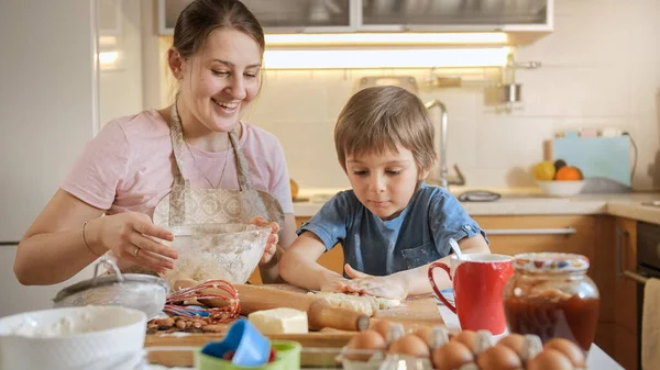 Młoda matka z małym synem ugniatająca ciasto i formująca je na drewnianą deskę. Dzieci gotujące z rodzicami, mały kucharz, rodzina spędzająca razem czas, kuchnia domowa. — Zdjęcie stockowe