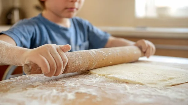 Крупный план маленького мальчика со скалкой, делающей тесто и готовящей на домашней кухне — стоковое фото