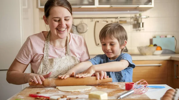 Счастливая улыбающаяся мать с сыном катит тесто для пиццы на кухне — стоковое фото