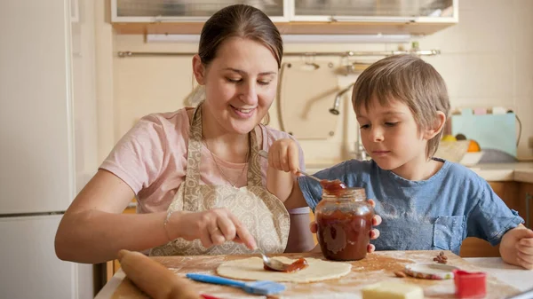 Uśmiechnięta matka z małym synkiem wypełniającym ciasto lub ciasto słodką jamą.Children gotowania z rodzicami, mały kucharz, rodzina mając czas razem, kuchnia domowa — Zdjęcie stockowe