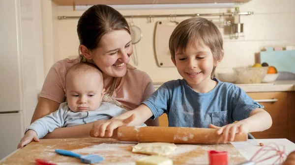 Ευτυχισμένη οικογένεια με παιδιά να κυλούν ζύμη για μπισκότα ή πίτα στην κουζίνα. Παιδιά μαγείρεμα με τους γονείς, λίγο σεφ, οικογένεια έχοντας χρόνο μαζί, οικιακή κουζίνα. — Φωτογραφία Αρχείου