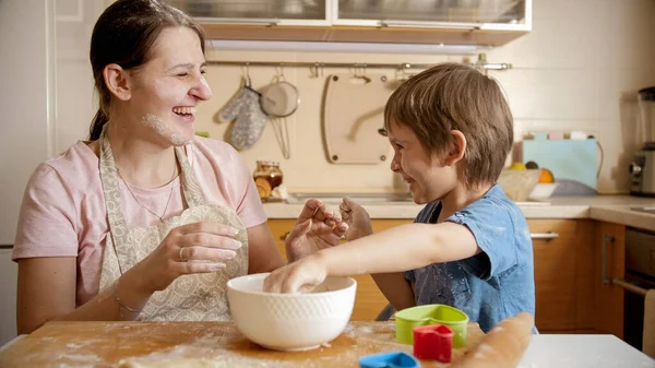 Tertawa ibu dengan anak melemparkan tepung satu sama lain sambil memasak di rumah. Anak-anak memasak dengan orang tua, koki kecil, keluarga memiliki waktu bersama-sama, dapur domestik. — Stok Foto