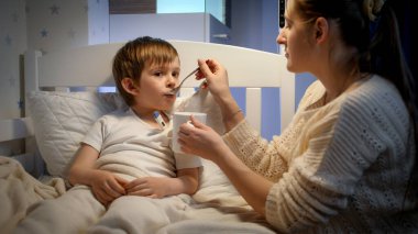 Küçük hasta çocuk kendini kötü hissediyor. Yatakta yatıp, kaşıktan ilaç ve şurup içiyor. Çocuk hastalığı, hastalık ve ebeveyn bakımı kavramı