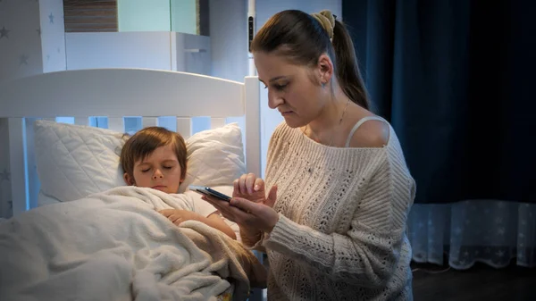 Madre joven preocupada por su hijo enfermo durmiendo en la cama llamando al médico. Concepto de enfermedad infantil, enfermedad y cuidado de los padres. —  Fotos de Stock