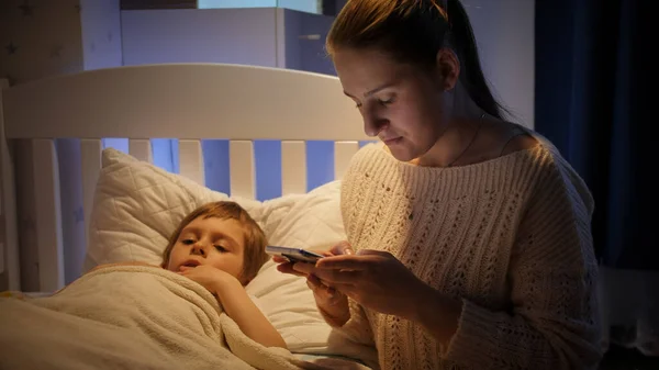 Genç anne gece akıllı telefondan hasta çocuk için ilaç arıyor. — Stok fotoğraf