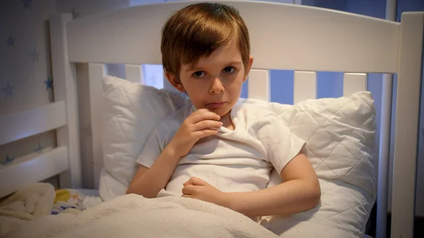 Menino doente deitado na cama e a medir a temperatura corporal com o termómetro. Conceito de doença infantil, doença e cuidados de saúde — Fotografia de Stock