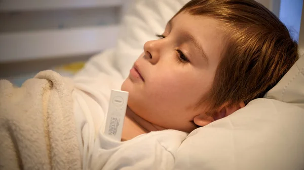 Retrato de menino doente deitado na cama e medindo a temperatura com termômetro — Fotografia de Stock