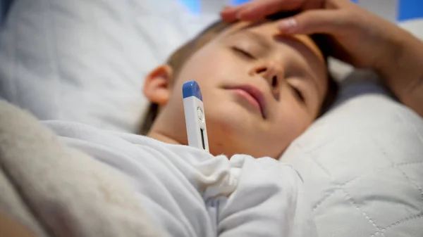 Fechar a mão das mães acariciando seu filho doente deitado na cama e medir a temperatura corporal. Conceito de doença infantil, doença e cuidado dos pais — Fotografia de Stock