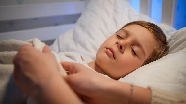 Mère attentionnée ajustant la couverture et embrassant son petit fils endormi la nuit. Concept de parentalité et de bonheur familial. — Photo