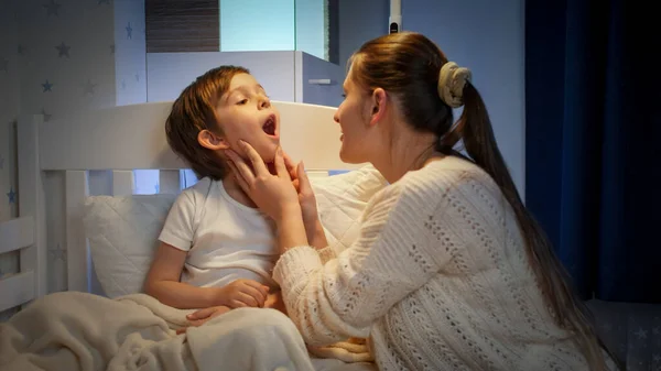 Chłopiec cierpiący na ból gardła, otwierający usta i pokazujący je matce w nocy. Pojęcie choroby dzieci, choroby i opieki rodzicielskiej — Zdjęcie stockowe