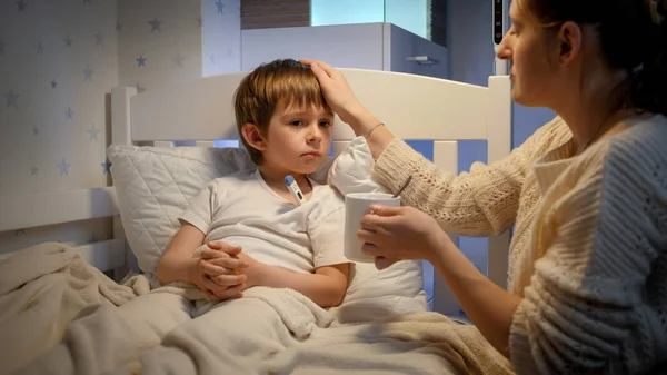 Mère attentionnée touchant le front de son enfant malade couché au lit — Photo