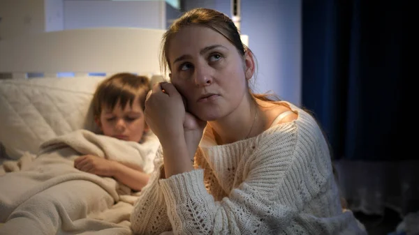 Chorando mãe sentada ao lado da cama de seu filho pequeno à noite — Fotografia de Stock