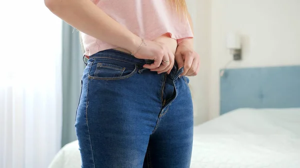 Mujer joven con caderas anchas y vientre poniéndose jeans ajustados y luchando para abotonarlos. Concepto de exceso de peso, obesidad femenina, dieta y problemas de sobrepeso — Foto de Stock