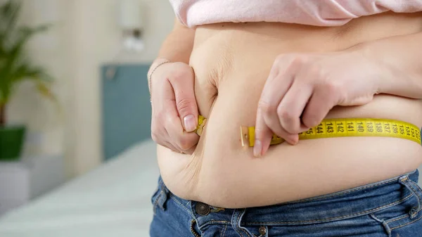 Молодая женщина страдает от избыточного веса, измеряя свой большой живот. Концепция питания, нездорового образа жизни, избыточного веса и ожирения — стоковое фото