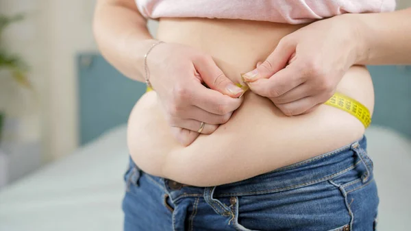 Mladá žena stojí v ložnici a měří pas. Koncepce diety, nezdravého životního stylu, nadváhy a obezity — Stock fotografie