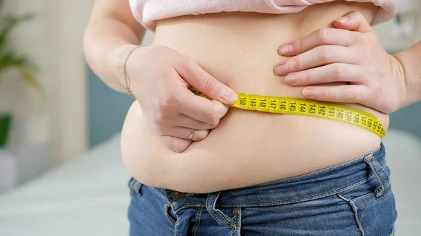 Closeup of overweight woman using measuring tape. Concept of dieting, unhealthy lifestyle, overweight and obesity