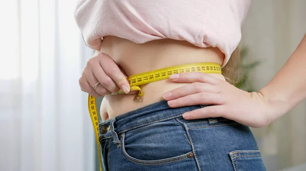 Mladá žena v džínách měří štíhlý plochý pas měřicí páskou. Koncepce stravy, hubnutí a zdravého životního stylu. — Stock fotografie
