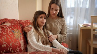 Genç kızlar ağlayan üzgün kız arkadaşını okşayıp teselli ediyorlar. Arkadaş desteği ve ergen depresyonu