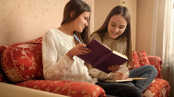 Zwei glücklich lächelnde Mädchen, die lächeln und lachen, während sie Hausaufgaben machen und in Textbücher oder Tagebücher schreiben — Stockfoto