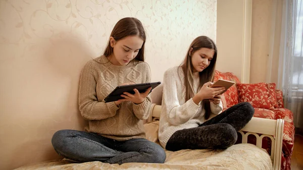 Yatakta oturup tablet bilgisayar kullanan iki genç kız. Evden eğitim ve yeni öğrenme teknolojisi. — Stok fotoğraf