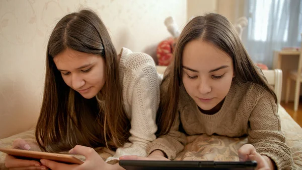 Две сестры используют таблетки на кровати. Подростки учатся и пользуются современными гаджетами дома — стоковое фото