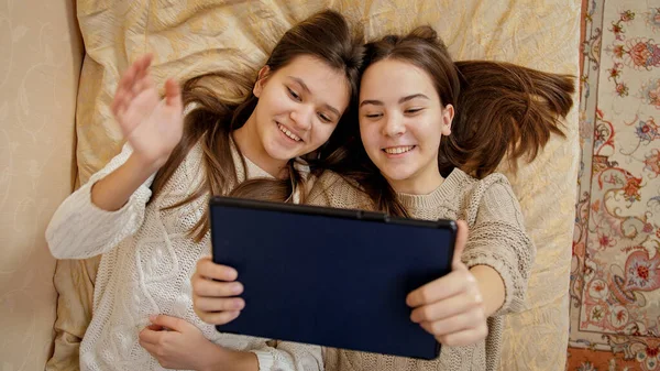 Vista superior de dos niñas acostadas en la cama y el uso de la tableta. Estudio remoto y comunicación desde el hogar —  Fotos de Stock