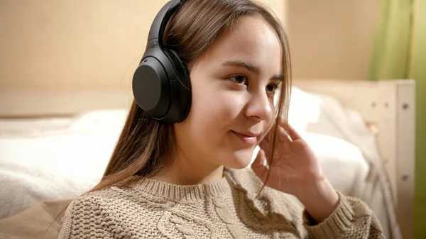 Портрет усміхненої дівчини-підлітка, яка насолоджується прослуховуванням музики в навушниках у спальні . — стокове фото