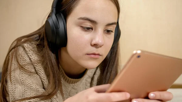 Menina adolescente morena em fones de ouvido deitado na cama e usando o computador tablet — Fotografia de Stock