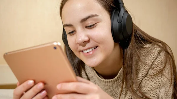 Smiling teenage girl with tablet computer lying on bed and listening music in headphones — Stock Photo, Image