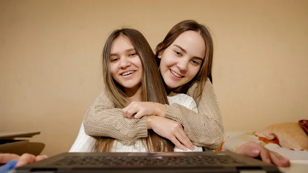 Dos adolescentes sonrientes tienen videollamada en la computadora portátil en casa. Trabajo remoto, comunicación y educación —  Fotos de Stock