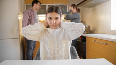 Bağrışmalar ve arka planda tartışmalar yüzünden elleri kulaklarını tıkayan genç bir kız. Aile içi şiddet, çatışmalar ve ilişki sorunları