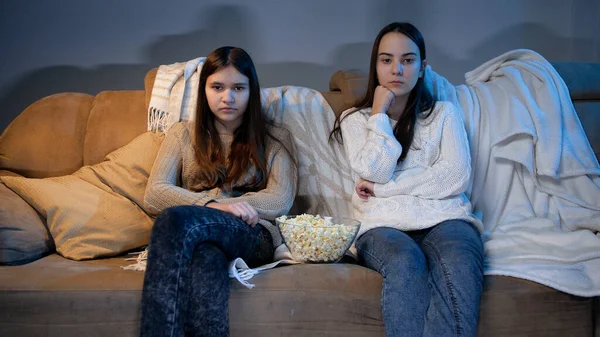 Duas adolescentes assistindo TV no sofá e comendo pipocas à noite — Fotografia de Stock