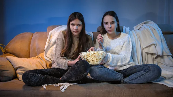 Duas meninas concentradas assistindo TV no sofá e comendo pipocas de tigela grande — Fotografia de Stock