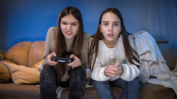 Δύο συμπυκνωμένα κορίτσια που παίζουν βιντεοπαιχνίδια στην κονσόλα παιχνιδιών στο σαλόνι τη νύχτα — Φωτογραφία Αρχείου