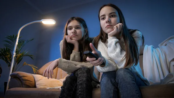 Two bored girls switching TV channels on remote controle while watching television at night — Stock Photo, Image