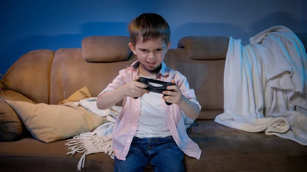 Engraçado menino segurando controlador de jogo enquanto joga jogos de vídeo no console de TV à noite — Fotografia de Stock